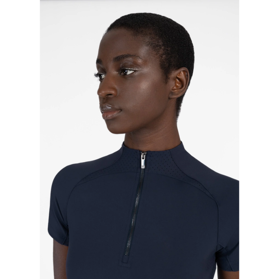 Model wearing black Maximilian Equestrian functional top on a white background, introducing the brand’s performance wear designed for movement in and out of the saddle.