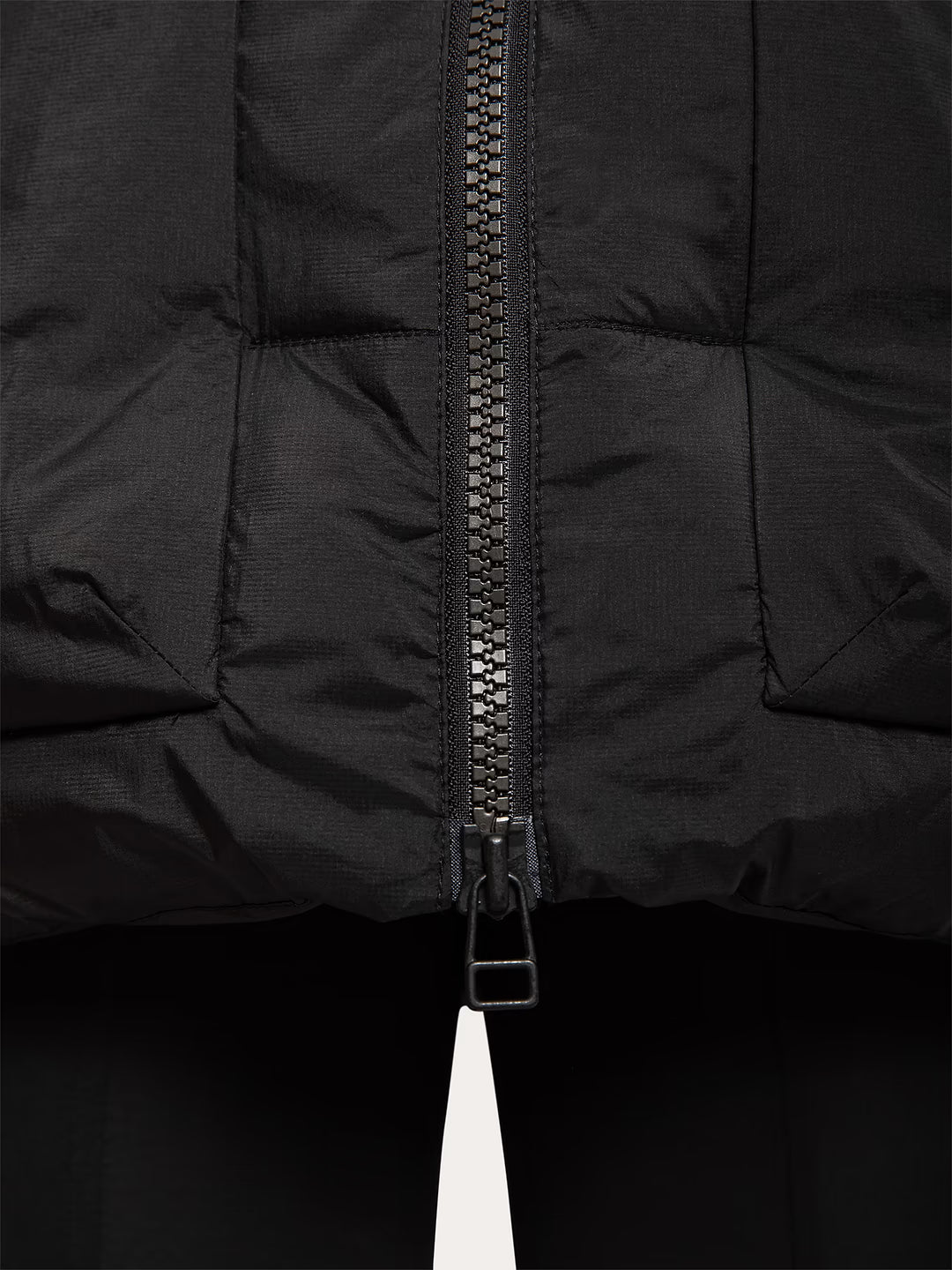 Close-up of a Uhip Arctic Puffer Jacket Jet Black with a central black zipper and a small white pull tab, shown against a dark background.