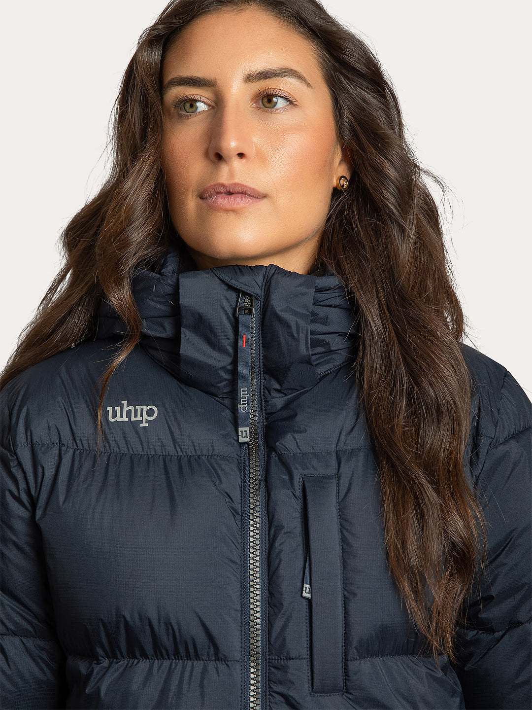A close-up of a woman wearing a Uhip arctic puffer coat extended eclipse with a high collar and a visible 'Uhip' logo on the left chest, set against a plain light background.