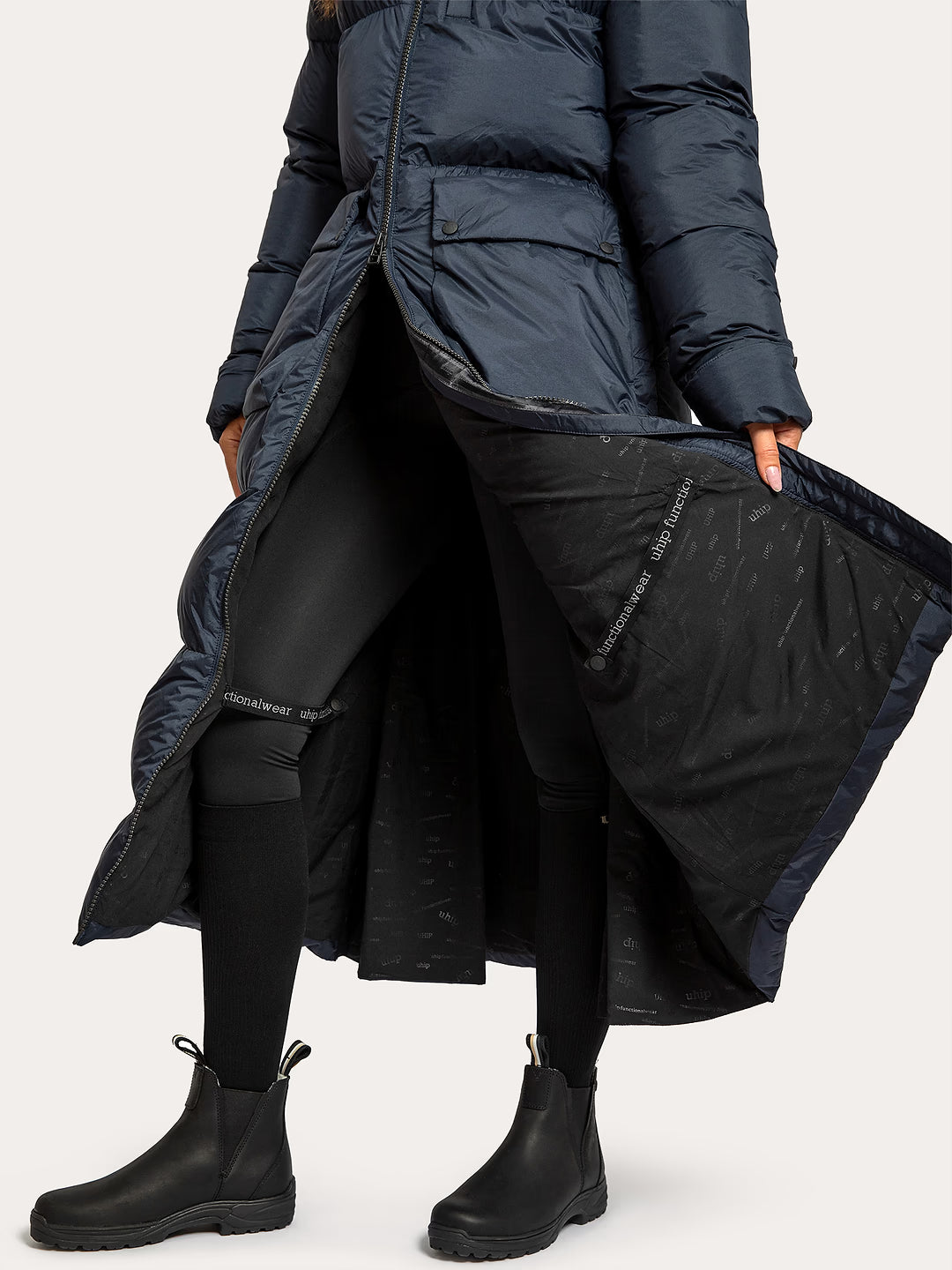 A model wearing a Uhip arctic puffer coat extended eclipse with a black interior lining, styled with black leggings and black Chelsea boots against a light grey studio background.