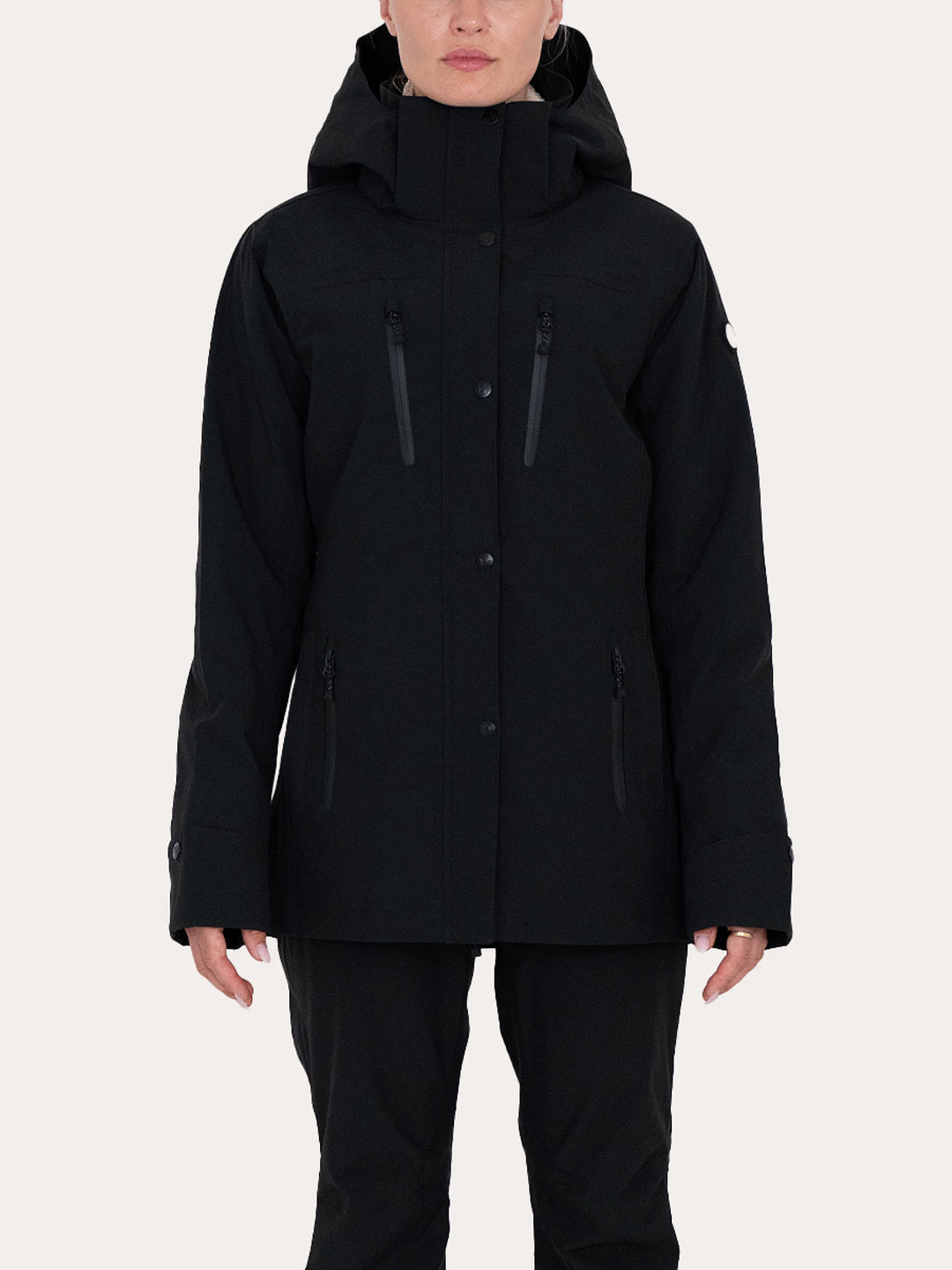 A model wearing a black Uhip Rainy Jacket with multiple zippered pockets, paired with black pants, against a solid light grey background.