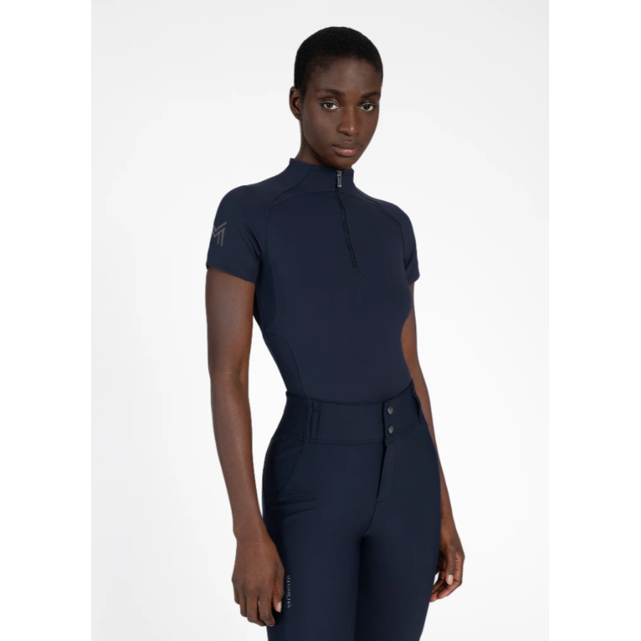 Model wearing black Maximilian Equestrian functional top on a white background, introducing the brand’s performance wear designed for movement in and out of the saddle.