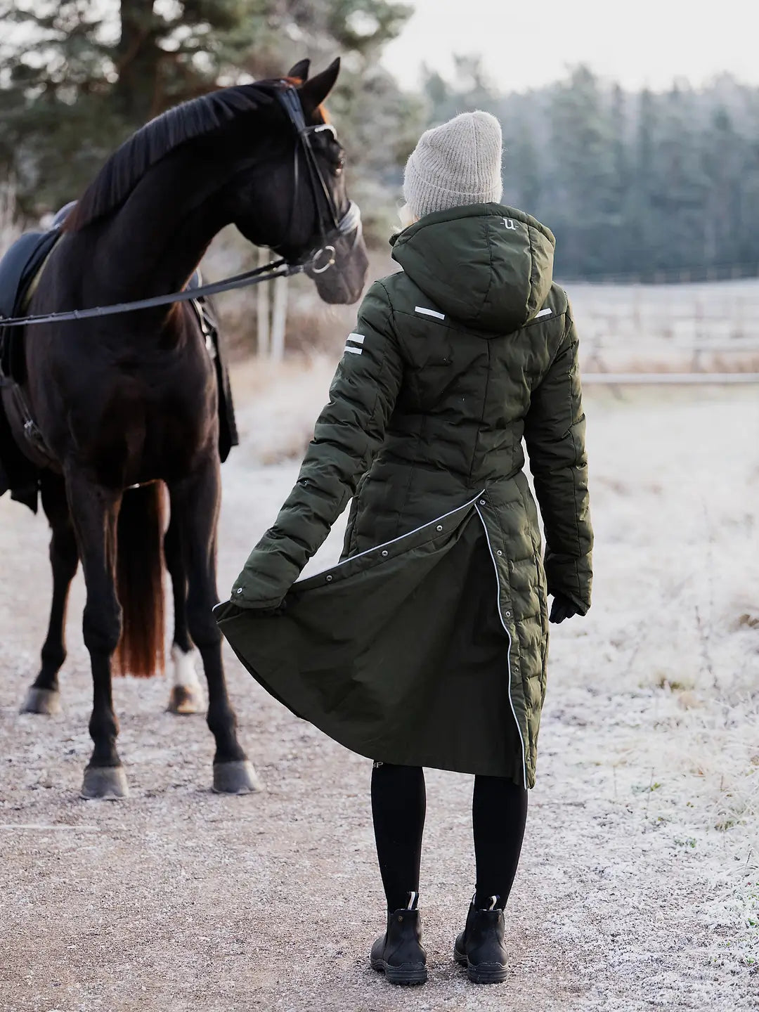 Person in a  Uhip Ice Coat in Dark Green standing next to a horse in a snowy landscape