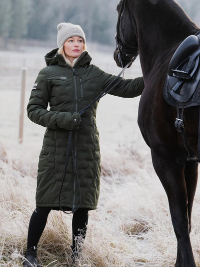Person in a Uhip Ice Coat in Dark Green standing next to a horse in a snowy landscape