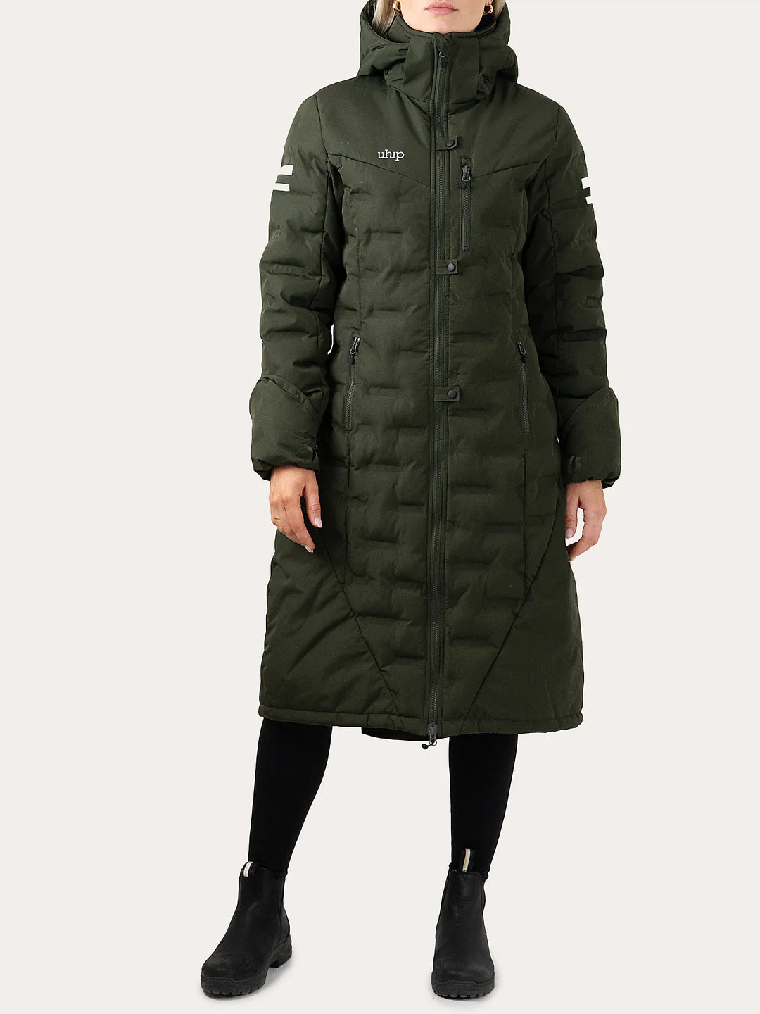 A model wearing a Uhip Ice Coat in Dark Green   with a hood, black leggings, and black boots, standing against a light grey studio background. The brand name 'Uhip' is visible on the left chest of the coat.