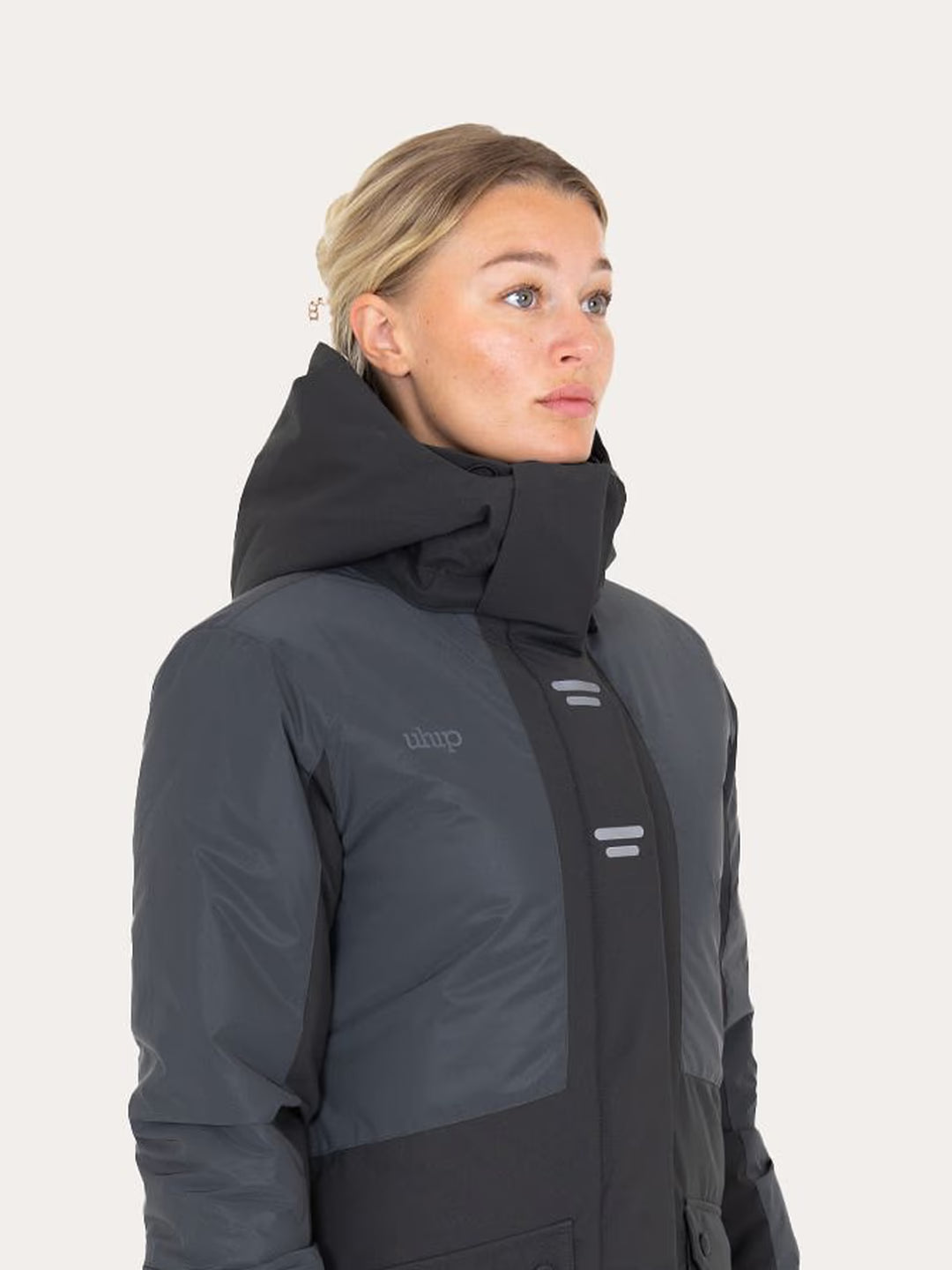 A woman wearing a Uhip Reflective Jacket 2.0  , shown in a side profile against a light off-white background.