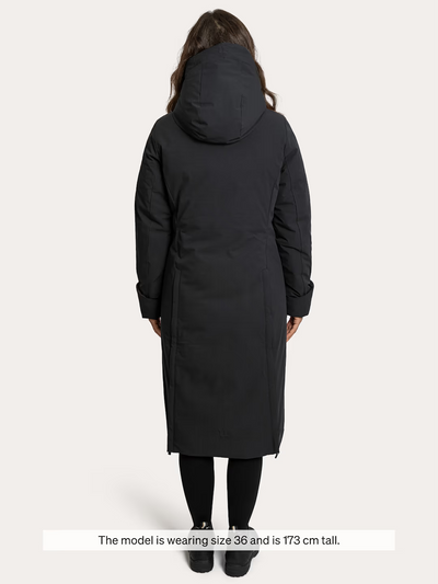 A woman shown from the back wearing a  Uhip Rime Coat 2.0 Dark Navy, black leggings, and black shoes against a light grey studio background. A text banner at the bottom reads, 'The model is wearing size 36 and is 173 cm tall.