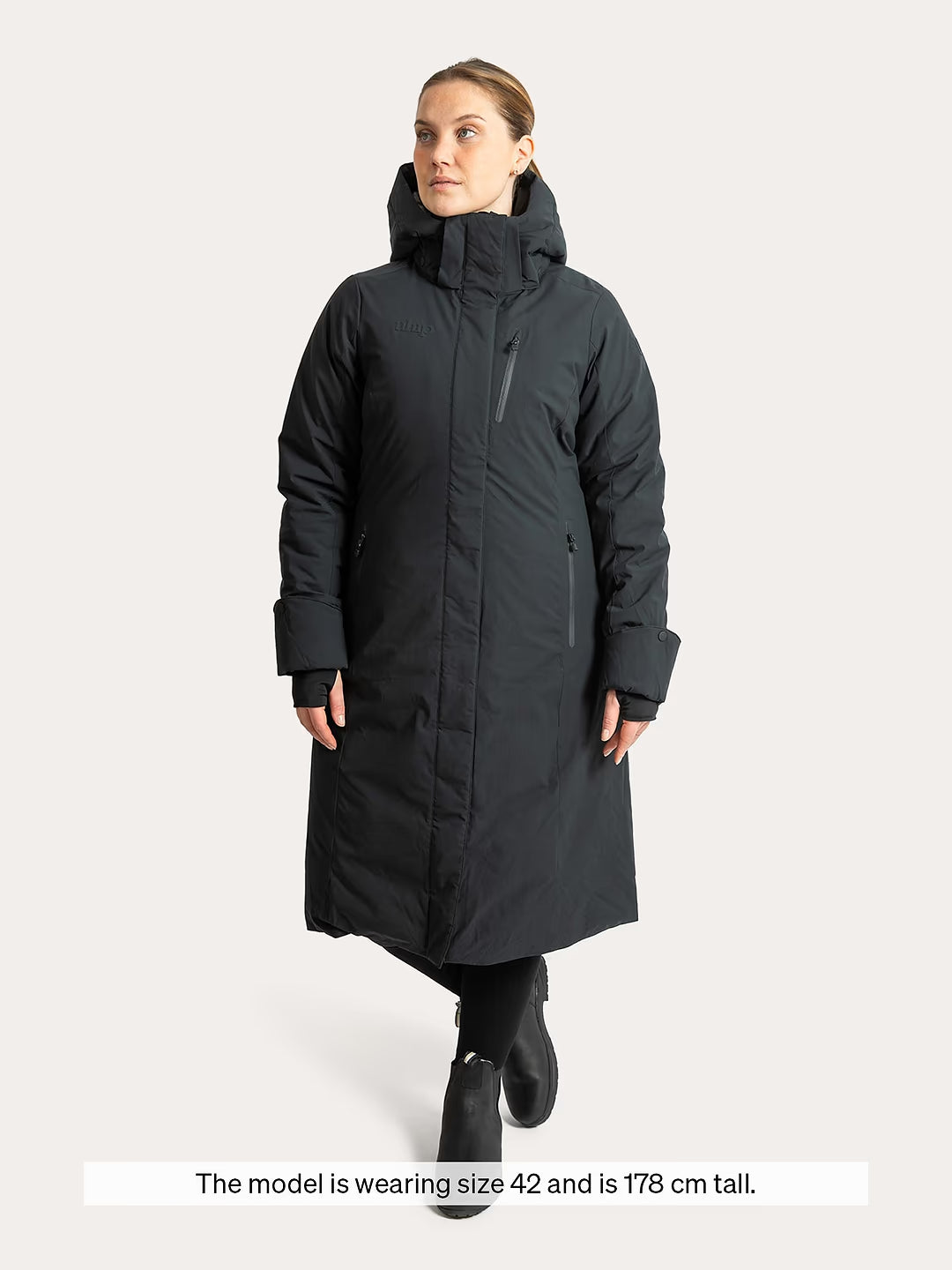 A woman modeling a Uhip Rime Coat 2.0 Dark Navy, against a light grey studio background. A text banner at the bottom reads, 'The model is wearing size 42 and is 178 cm tall.