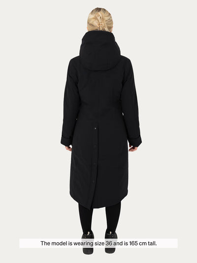 A woman viewed from the back wearing  Uhip Hailey Insulated Jet Black raincoat black leggings, and black shoes against a light gray studio background. A text banner at the bottom reads, 'The model is wearing size 36 and is 165 cm tall.