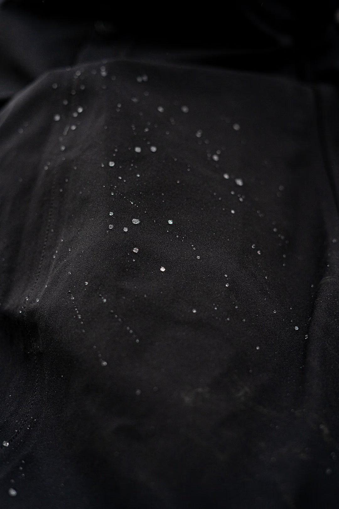 Close-up of a Uhip Hailey Insulated Jet Black raincoat black fabric surface with scattered small water drops