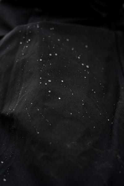 Close-up of a Uhip Hailey Insulated Jet Black raincoat black fabric surface with scattered small water drops
