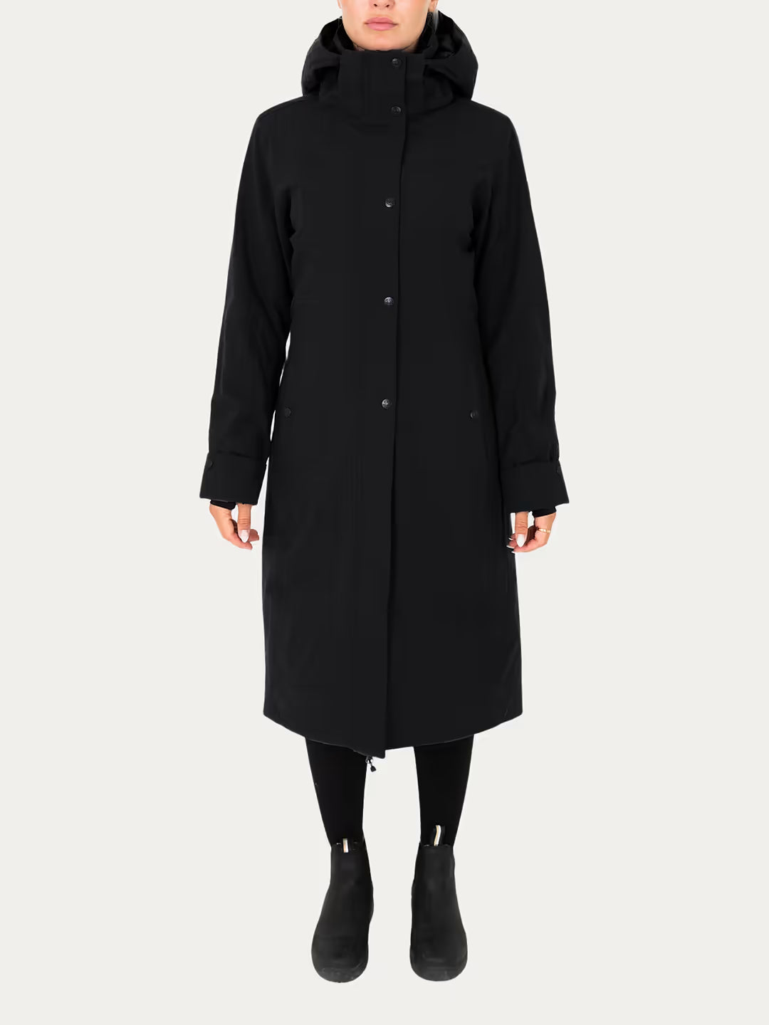 A model wearing a  Uhip Hailey Insulated Jet Black raincoat with front buttons, paired with black leggings and black ankle boots, against a light grey studio background.