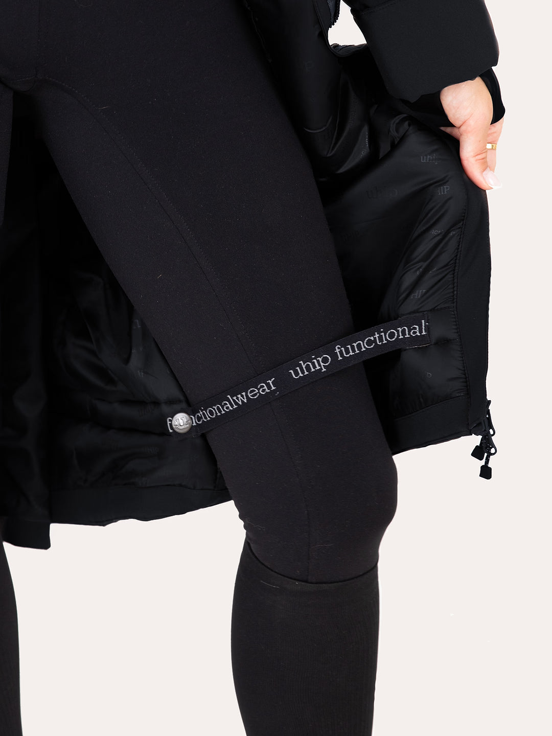 Close-up of a person wearing black athletic leggings and a Uhip Hailey Insulated Jet Black raincoat  showing a branded elastic band on the leg with the text 'Uhip functional wear'