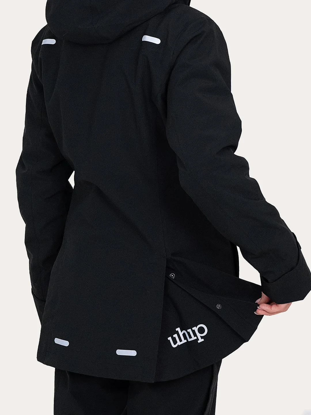 A close-up of a person wearing a black Uhip Rainy Jacket hooded jacket, shown from the back and side. The jacket has white reflective-looking tab details and a white 'uhip' logo near the lower back pocket area.