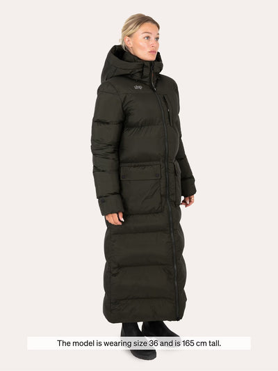 A woman modelling a with a Uhip arctic puffer coat extended dark green. and front zipper, shown against a light grey background with a size note at the bottom.